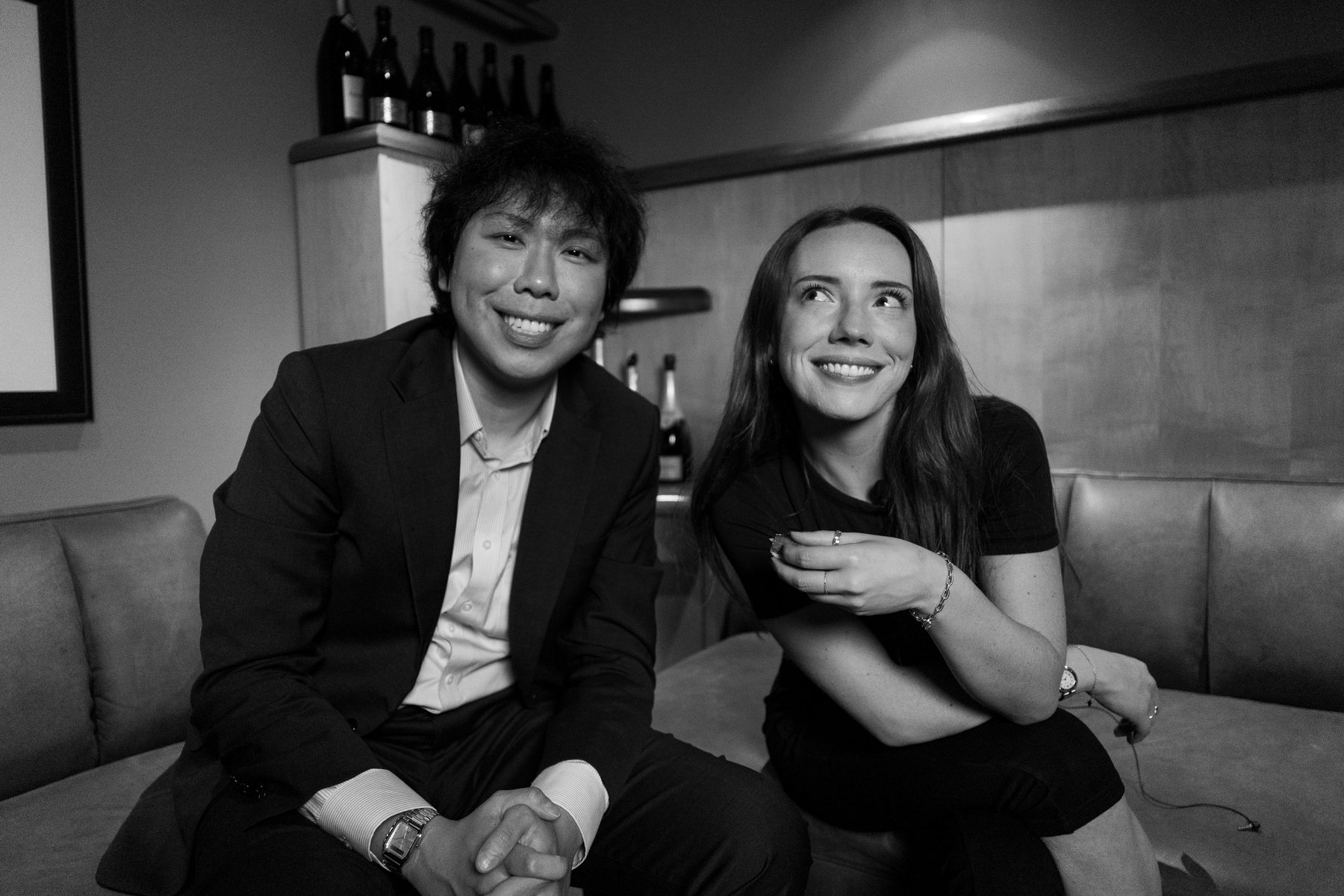 Ryan Deng and Autumn-Kyoko Cushman laughing on a leather banquette at the San Francisco Champagne Society.